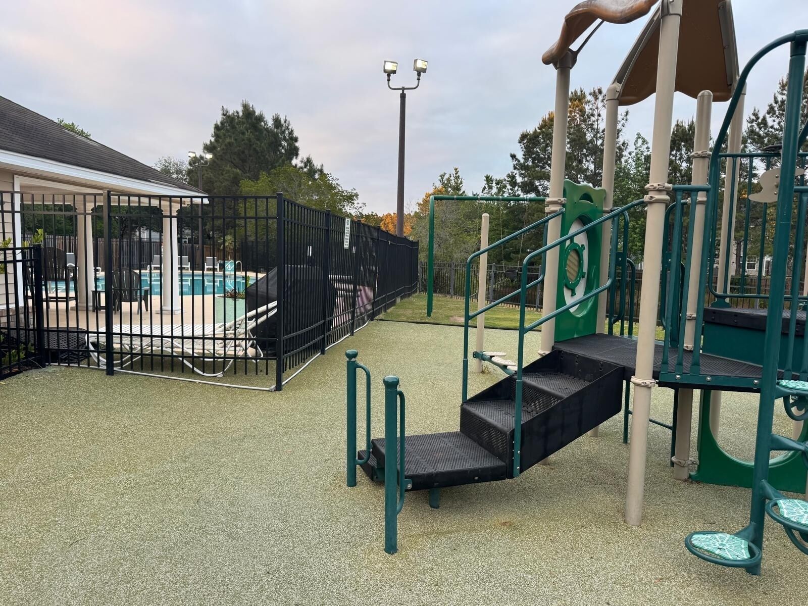 A playground with a climbing structure, a fenced pool area, and a covered seating area.