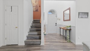 A hallway with a staircase, a white door, a console table with a plant, and a mirror on the wall. - Ideal Dream Getaway 4 Bedroom Home (Savannah)