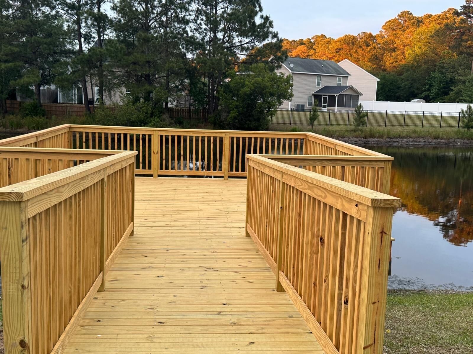 A wooden deck with railings, a body of water, and trees in the background.