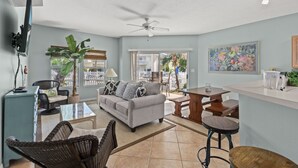 A living room with a sofa, chairs, a coffee table, a TV, and a ceiling fan. - Sandpiper Cove 9134 1 Bedroom Condo (Destin)