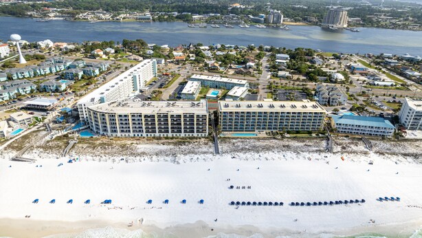 An aerial view of a coastal hotel with multiple buildings, a beach with umbrellas, and a view of the sea and cityscape. - Venus 119 1 Bedroom Condo (Fort Walton Beach)