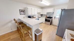 A modern kitchen with white cabinets, a stainless steel oven, and a wooden dining area. - Venus 119 1 Bedroom Condo (Fort Walton Beach)