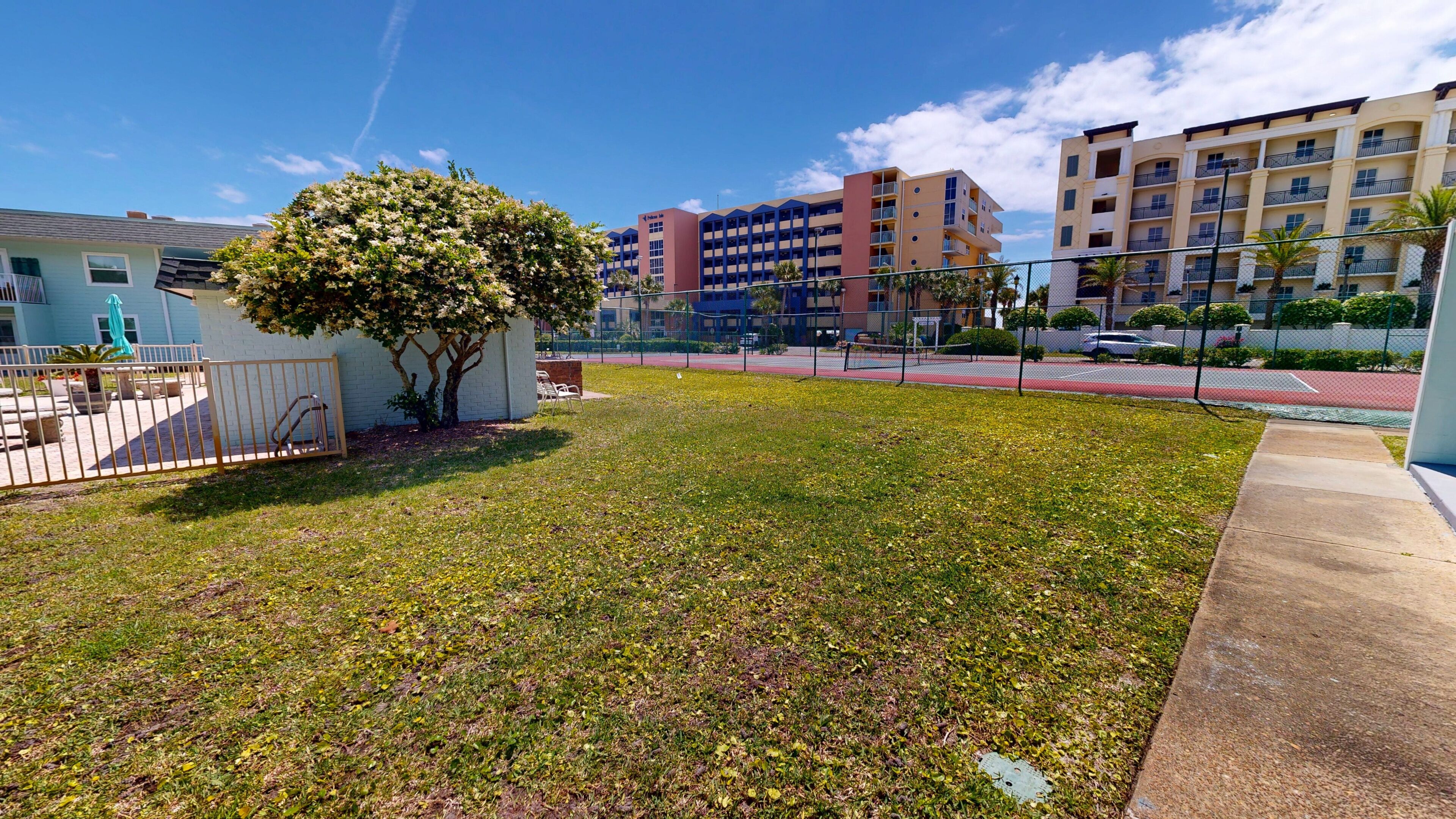 A residential area with a tree, a fenced yard, and apartment buildings in the background.