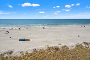 Ein weiter Sandstrand mit einigen Sonnenschirmen und Liegestühlen, einem blauen Rettungsschwimmerstand und dem Meer im Hintergrund.
