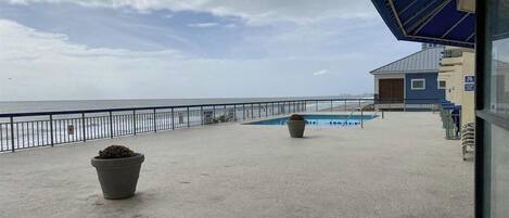Un balcone con vista sul mare, una piscina e un edificio con tetto blu.