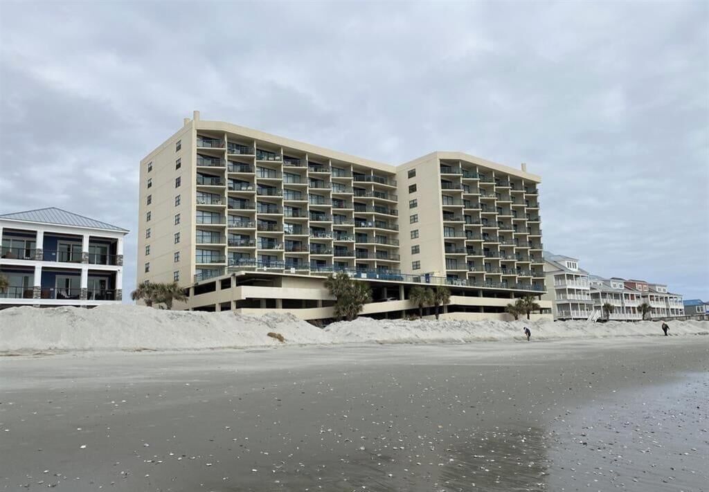 Un hotel de varios pisos con balcones, situado cerca de una playa con orilla arenosa.