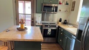 Een keuken met houten vloeren, groene kastjes, roestvrijstalen apparatuur en een centraal eiland met krukken.