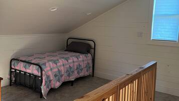 Ein Schlafzimmer mit schrägen Wänden, einem Bett mit gemustertem Überwurf, einem Hollaufstange und einem Deckenventilator.