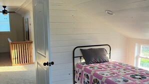 Een slaapkamer met een bed, een deur, een plafondventilator en een raam.