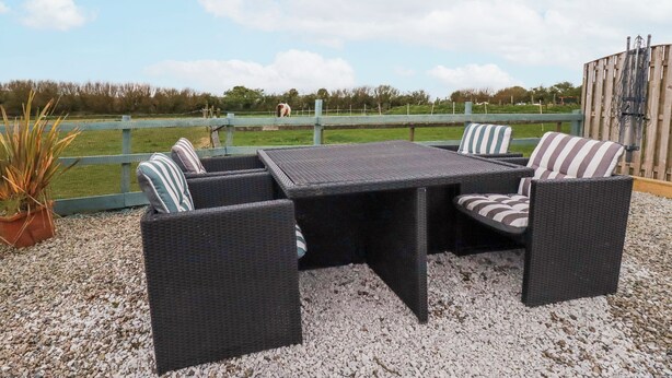 An outdoor seating area with wicker furniture and a view of a fenced field. - Moorland View (St Austell)