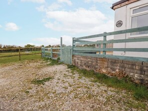 A gravel path leading to a gated area with a brick wall and a blue fence. - Moorland View (St Austell)