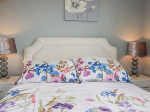 A bed with floral bedding, two bedside lamps, and a wall-mounted artwork. - Moorland View (St Austell)