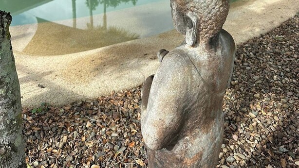 Una escultura de piedra en un jardín con piscina y sillones de descanso.