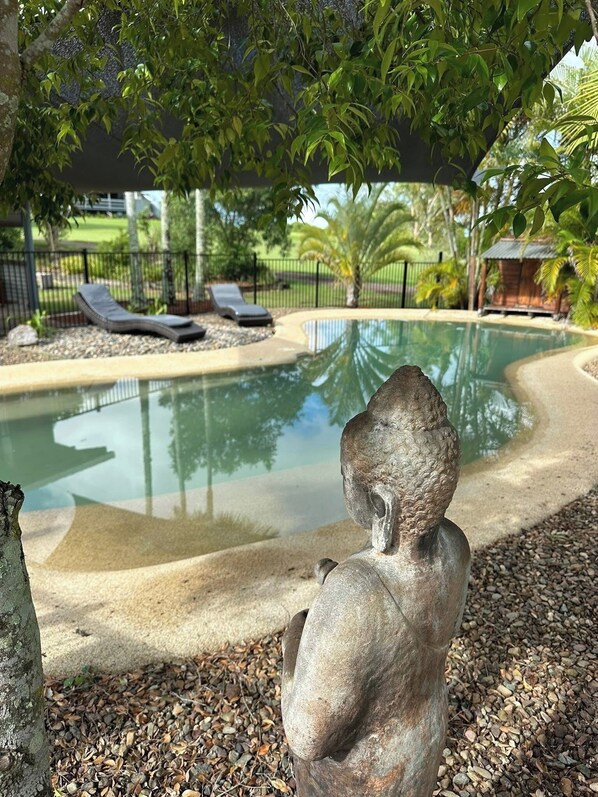 A stone sculpture in a garden with a pool and lounge chairs.