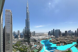 A high-rise building with a distinctive curved design, surrounded by a cityscape with modern architecture and a large, blue water feature. - Burj Khalifa Luxury 2BR - High Floor (Dubai)