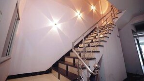 Una escalera con barandilla metálica y una pared con lámparas geométricas.