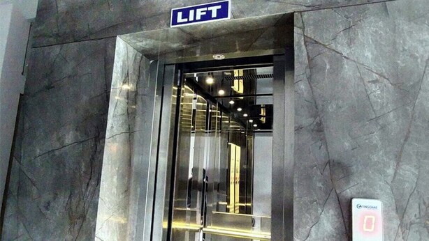 Entrada de ascensor con un cartel que dice 'LIFT', una pantalla digital y una pared de mármol.