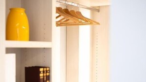 A white closet with shelves, a hanging rack, and a yellow vase. - A.Mare Hotel (Eraclea Mare)
