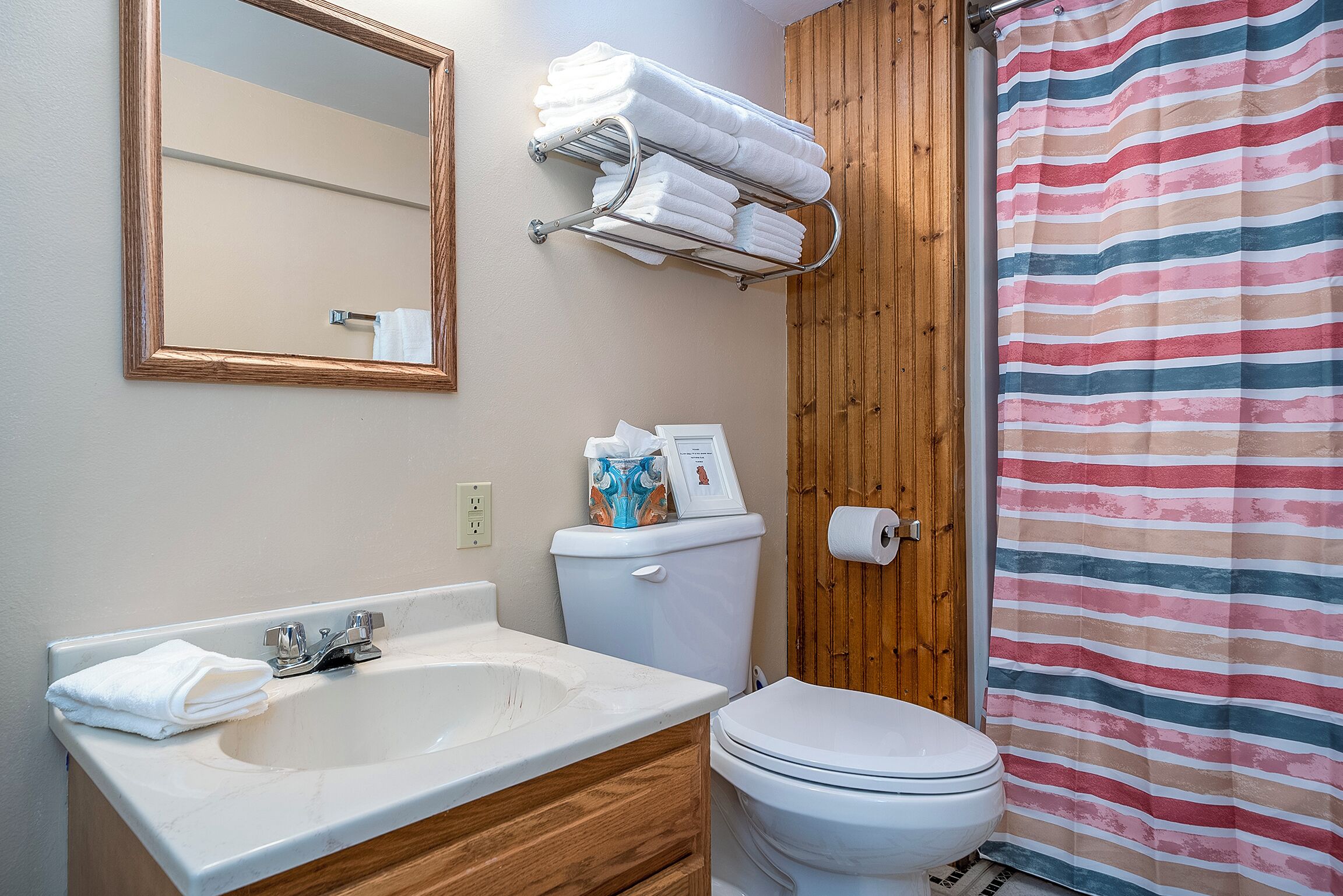 A bathroom with a sink, toilet, towel rack, and striped shower curtain.