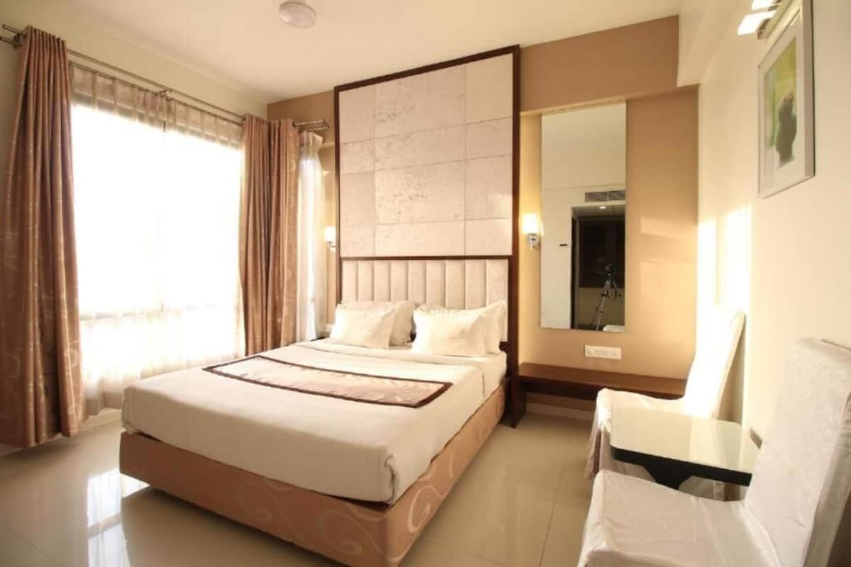 Una habitación de hotel con una cama grande, una silla, un espejo y una ventana con cortinas.