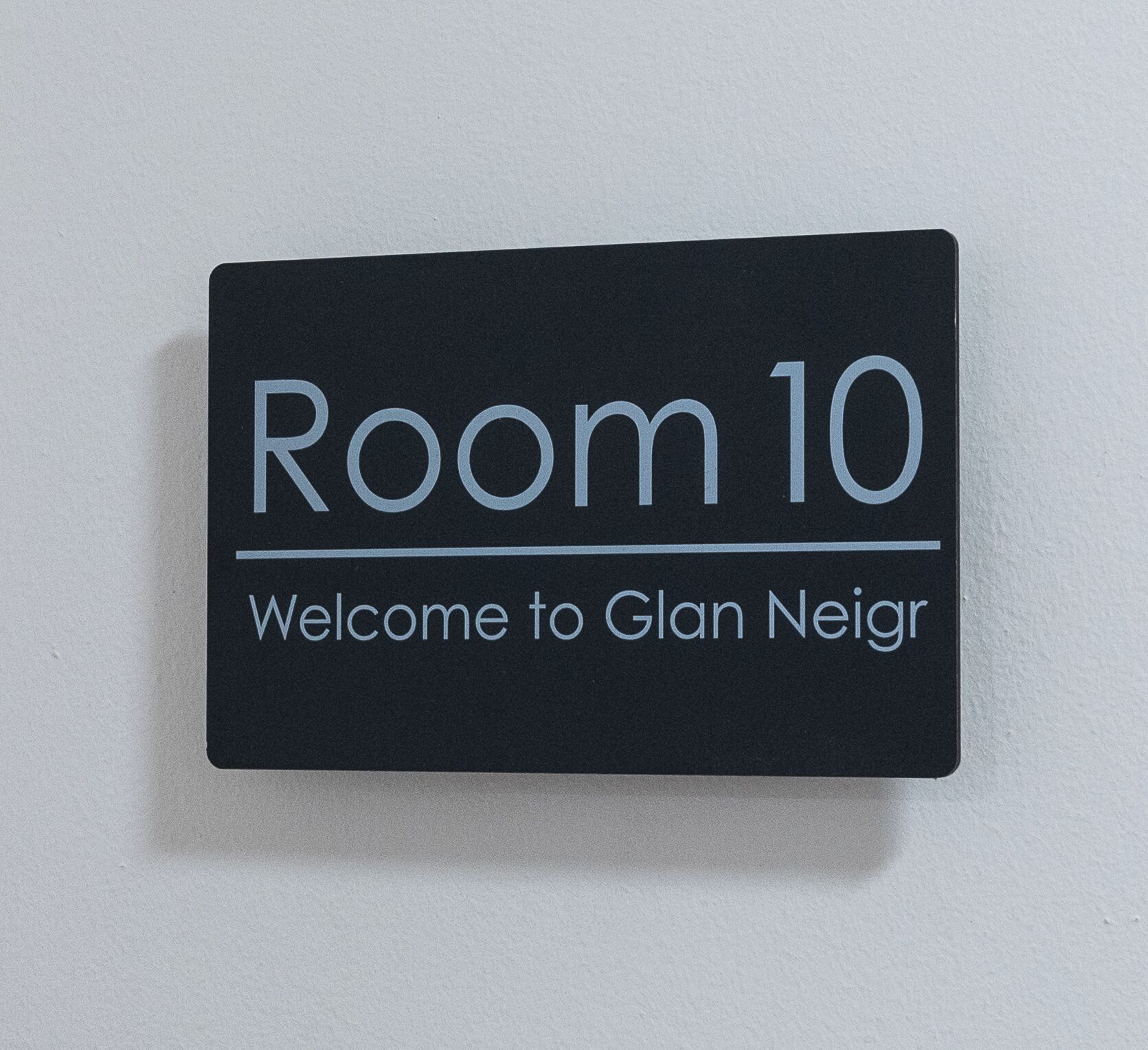 A sign with 'Room 10' and 'Welcome to Glan Neir' on a black background.
