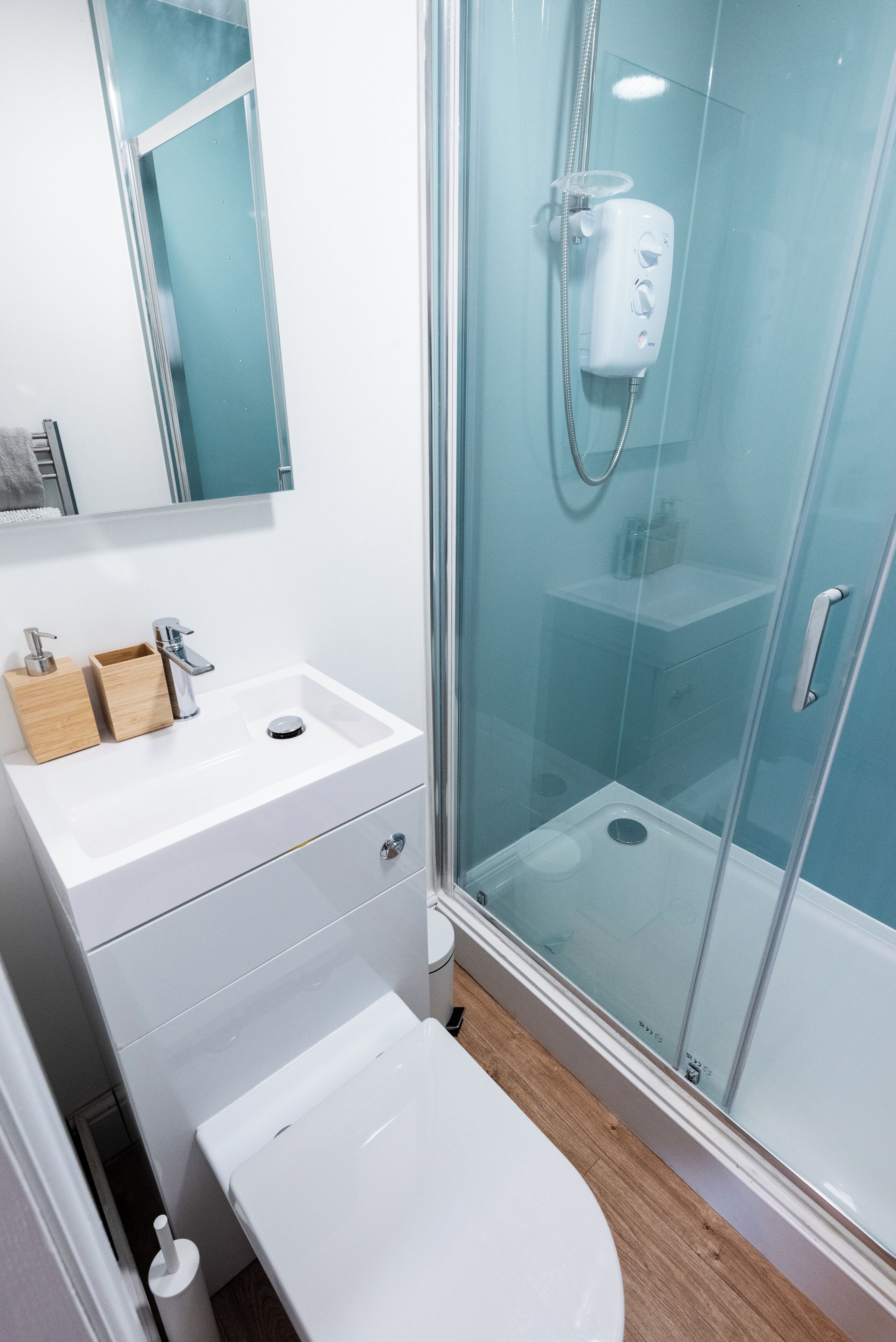A modern bathroom with a glass shower enclosure, a white sink with a wooden soap dish, and a toilet.