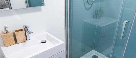 A modern bathroom with a glass shower enclosure, a white sink with a wooden soap dish, and a toilet.