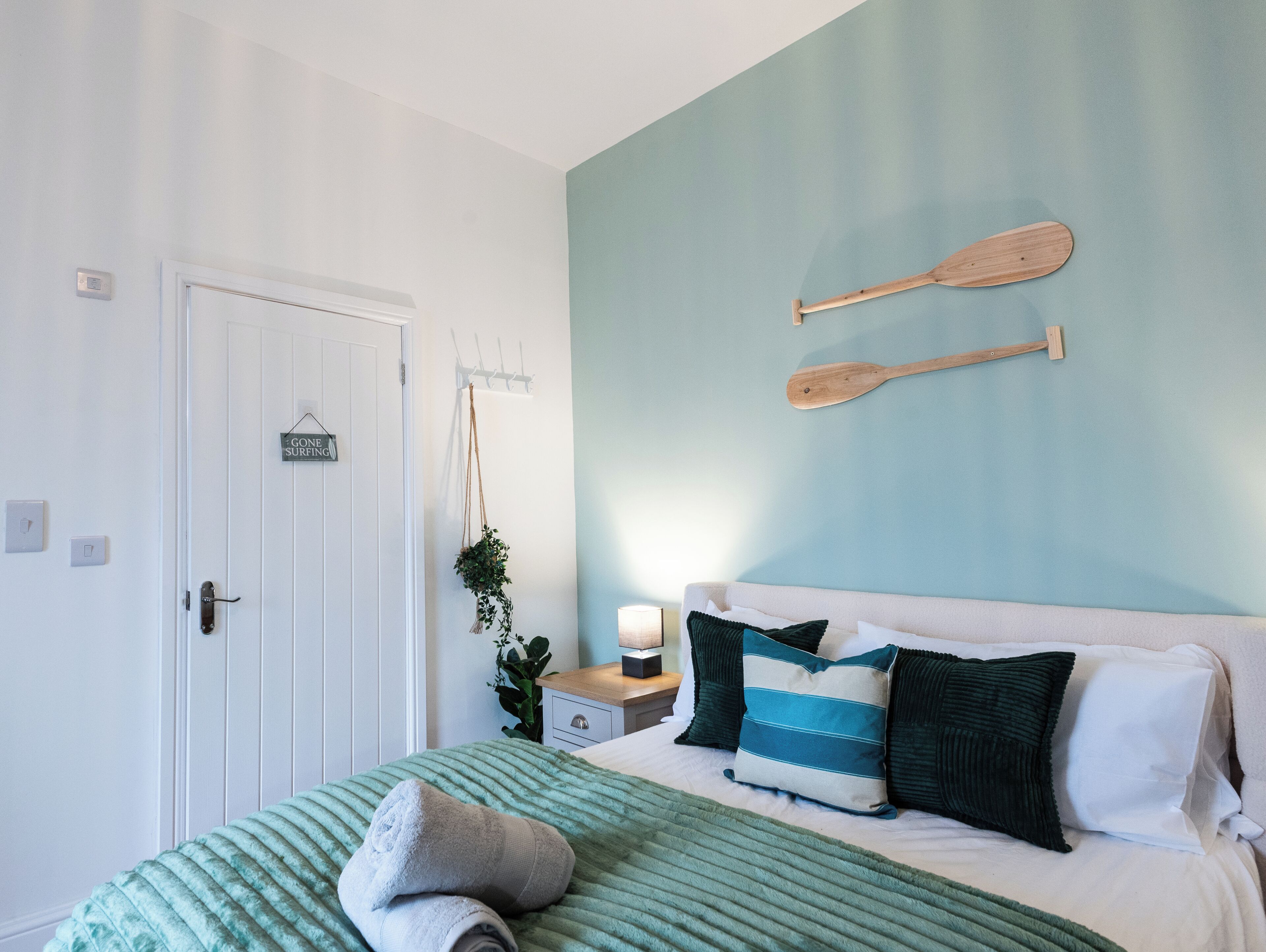 Una camera da letto con un letto, un comodino, una tavola da surf appesa al muro e una porta con un cartello.