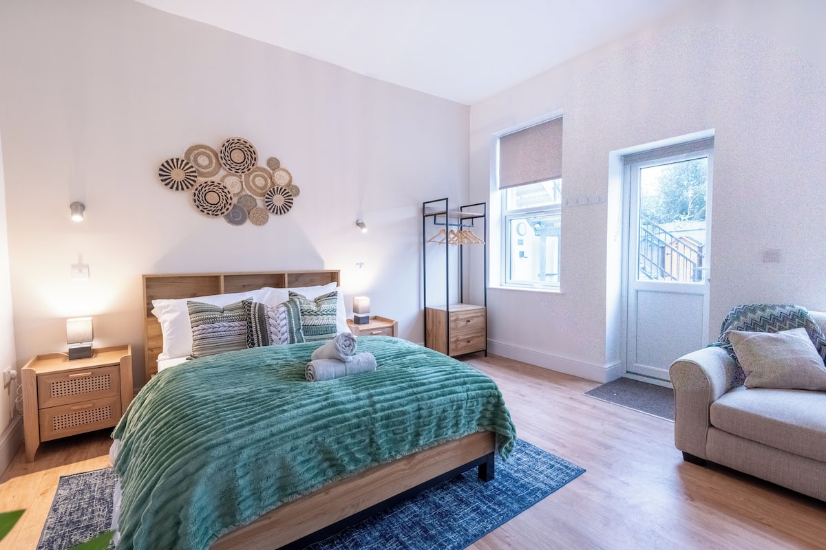 Un dormitorio con cama, mesitas de noche, cómoda, ventana y puerta.