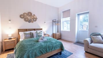 Quarto com cama, mesas de cabeceira, penteadeira, janela e porta.