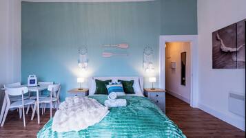 Un dormitorio con cama, mesitas de noche, escritorio, sillas y una pared decorada con atrapasueños.