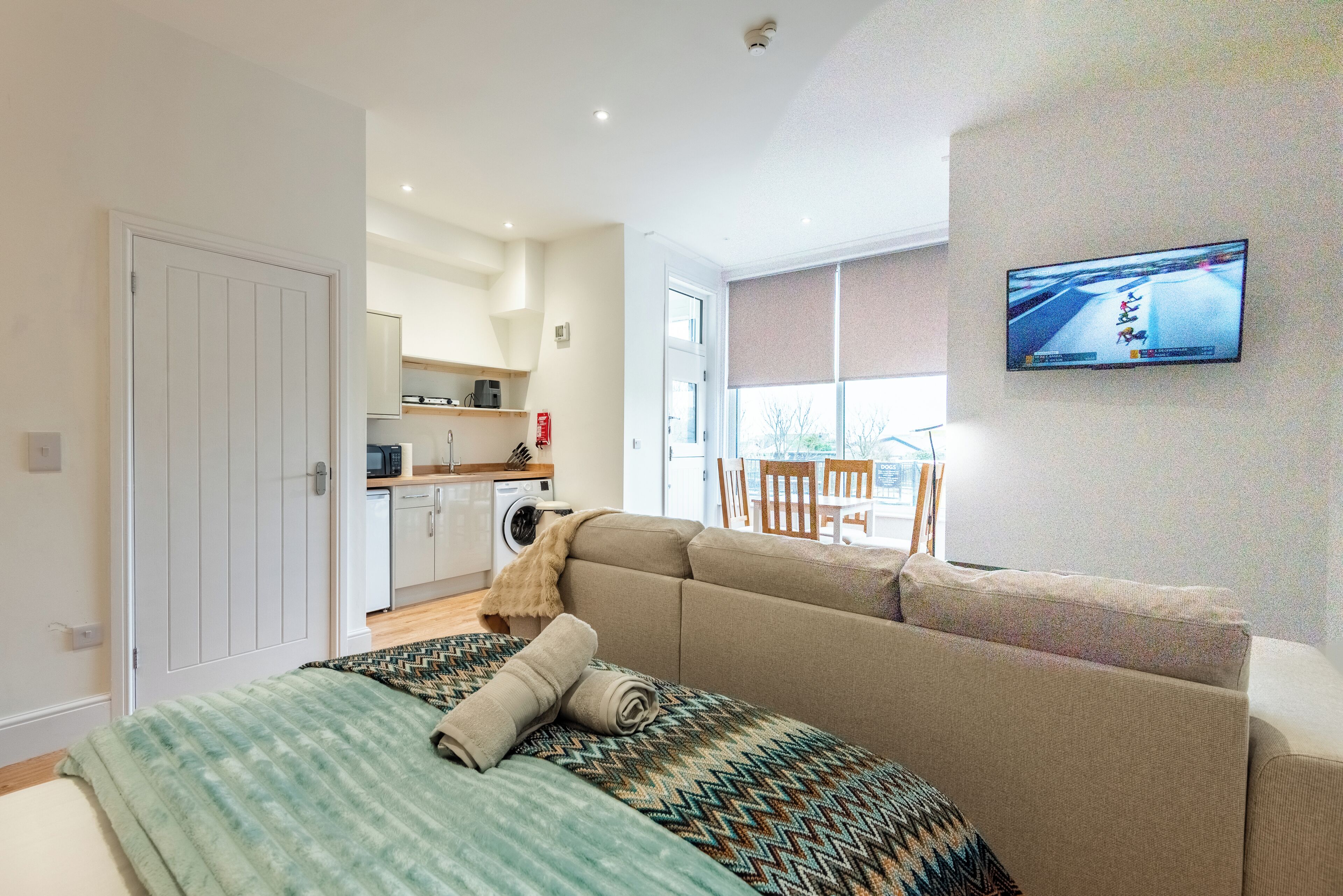 A modern room with a bed, a sofa, a television, a washing machine, and a dining area.