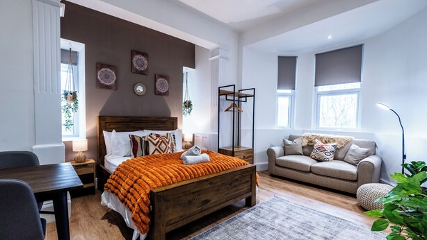 Un dormitorio con una cama de madera, un sofá, un escritorio y una planta colgante.