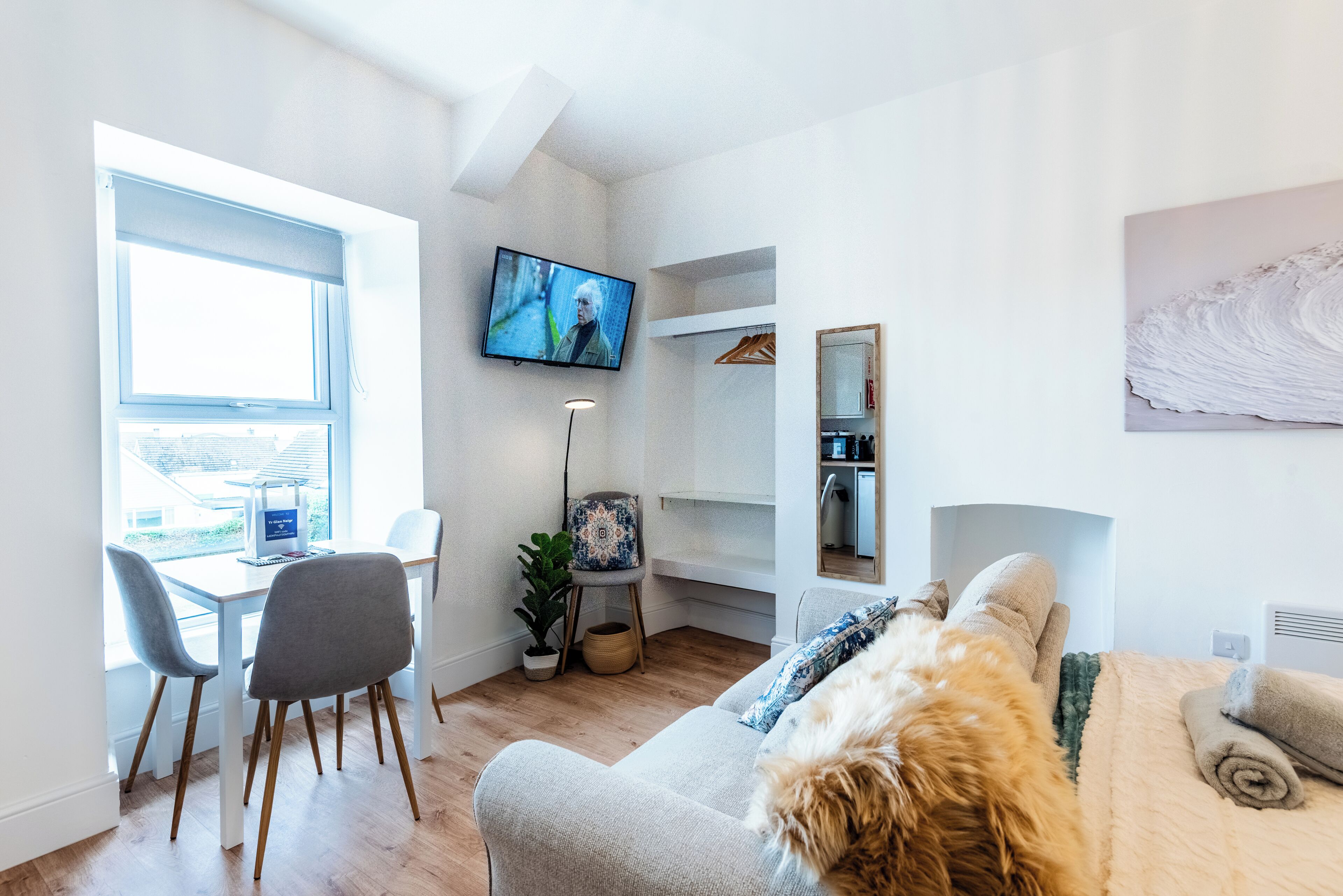 A modern living room with a sofa, a TV, a dining table with chairs, a plant, and a bookshelf.