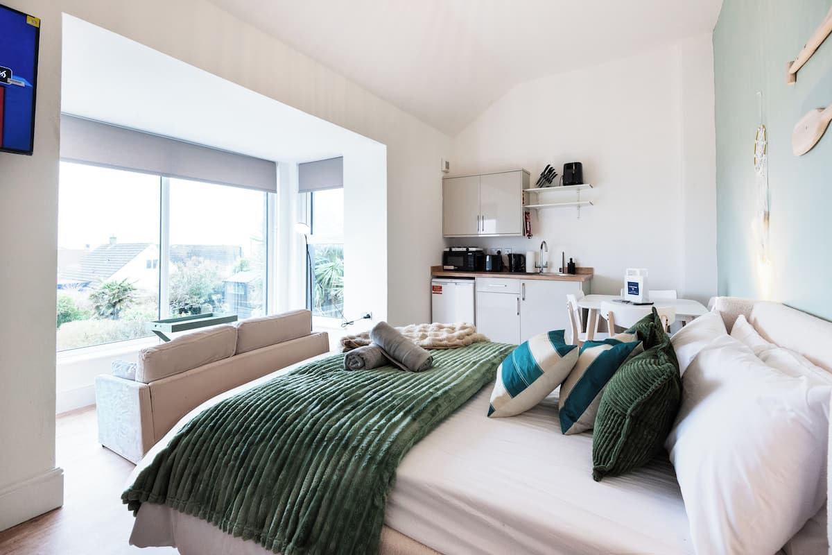 Un dormitorio moderno con una cama grande, un sofá, una cocina y vistas al exterior.