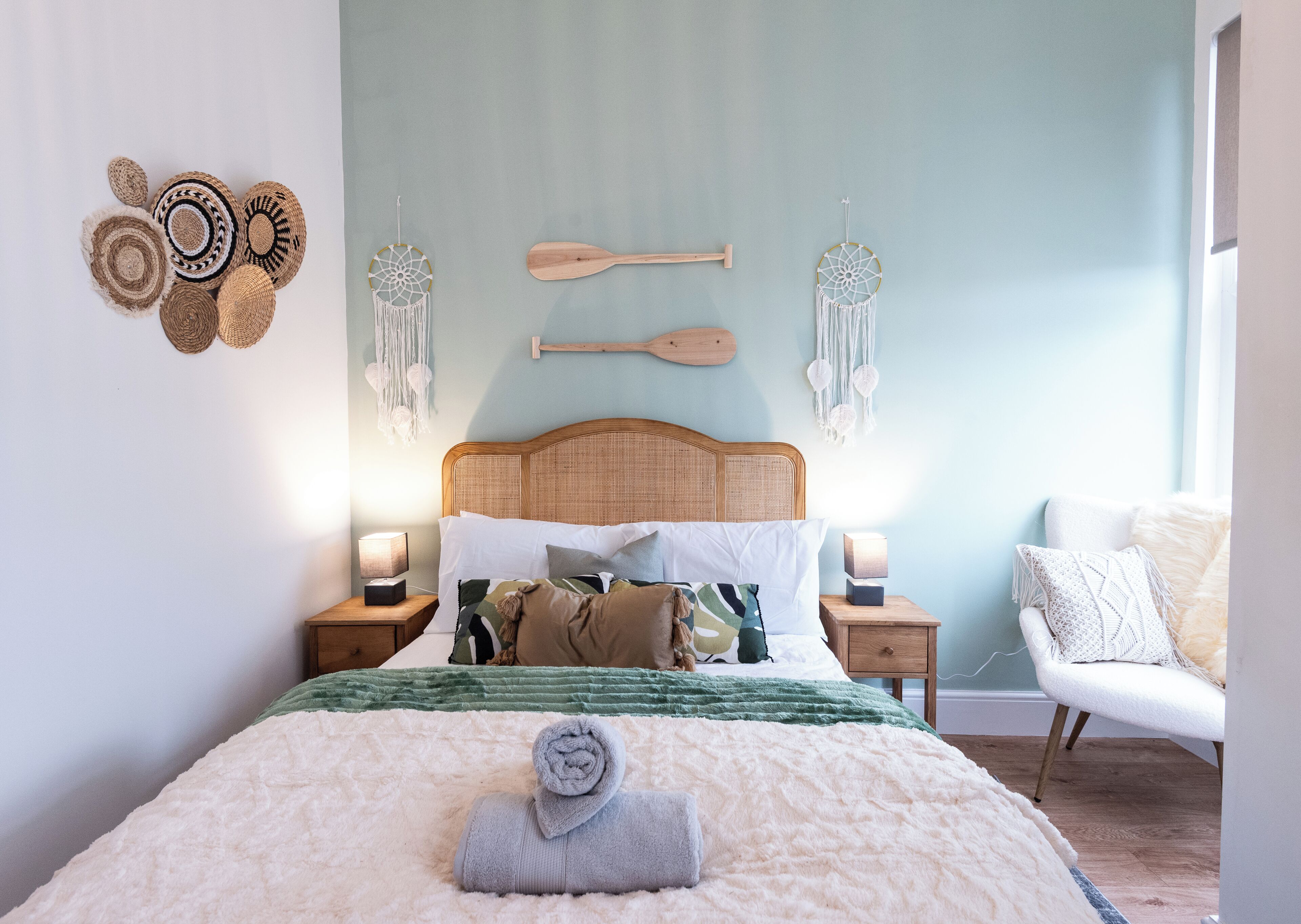 Un dormitorio con cama, mesitas de noche, una silla y adornos en la pared.