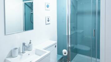 Un baño moderno con cabina de ducha de vidrio, un lavamanos blanco y un inodoro.