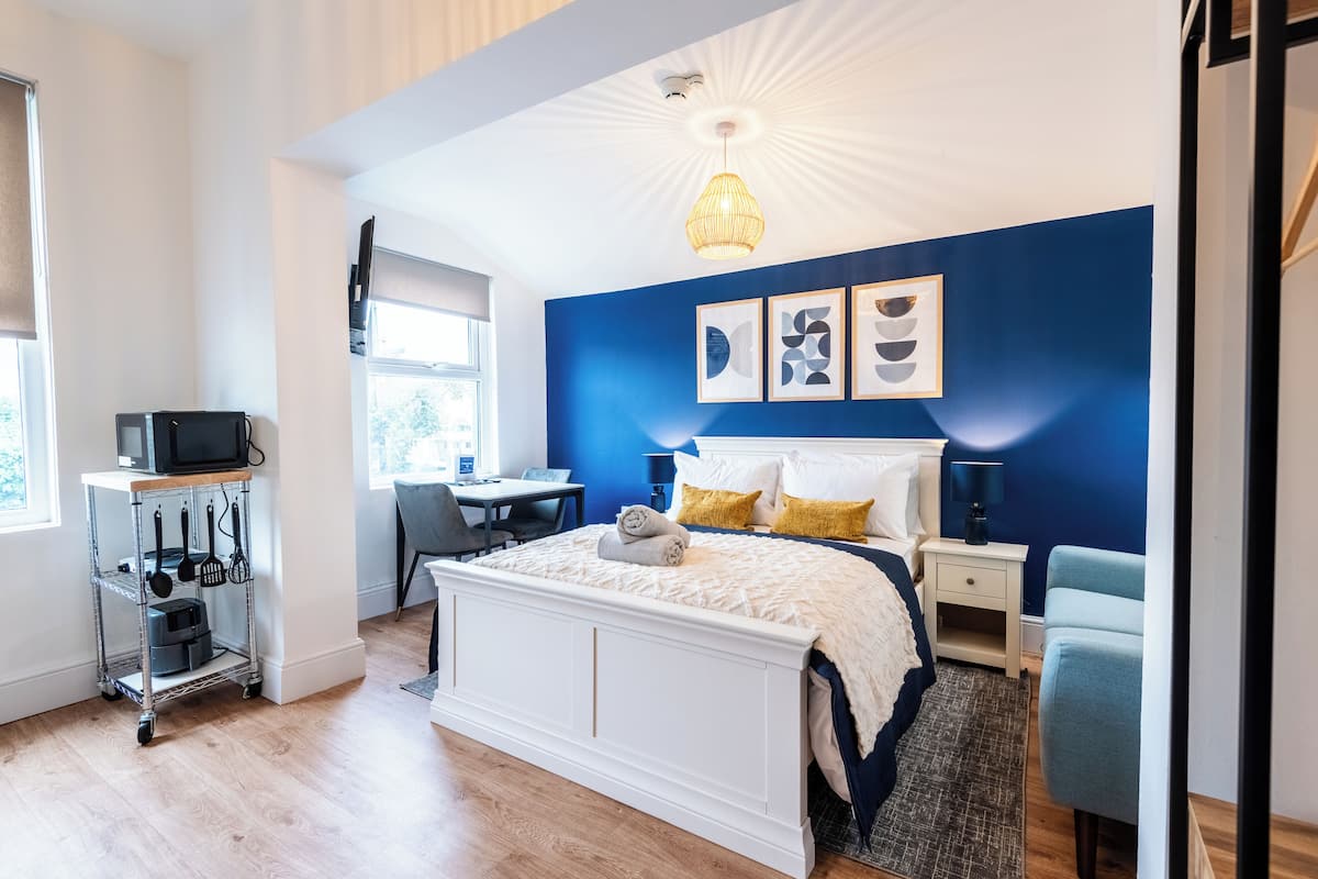 Un dormitorio moderno con una cama blanca, paredes de acento azul, un escritorio y un televisor en un estante.
