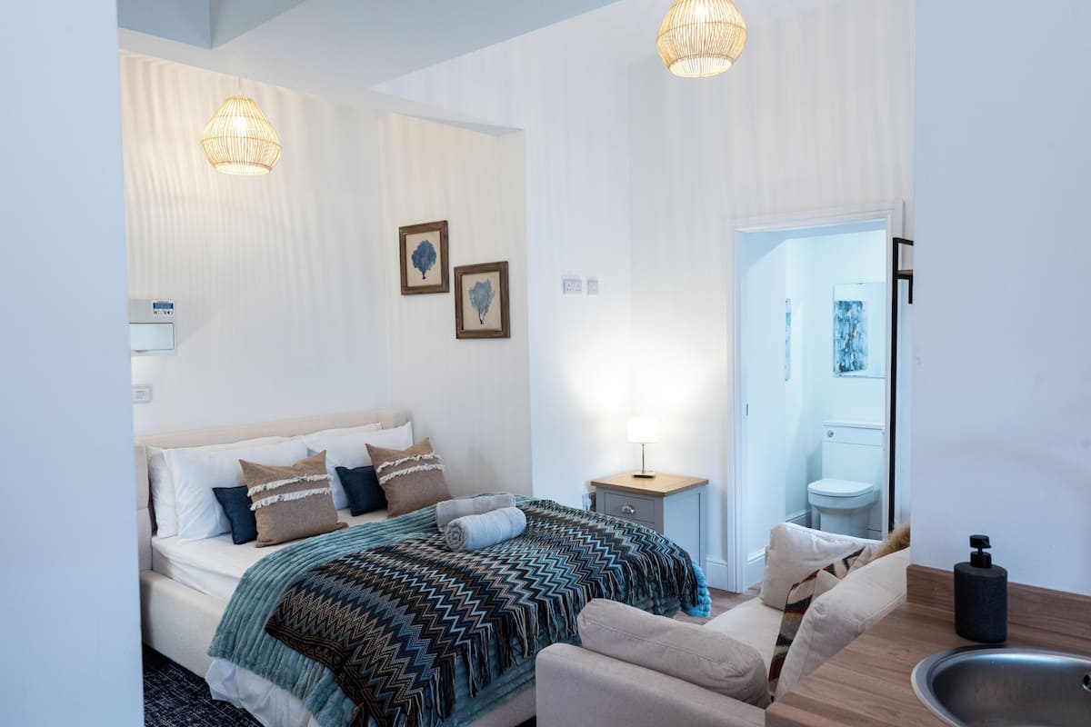 Un dormitorio moderno con cama, mesita de noche, lámpara y vistas al baño.