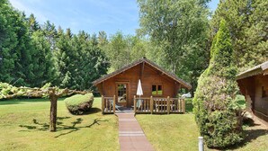 Une cabane en bois dotée d’un porche, entourée d’arbres et d’une zone herbeuse.