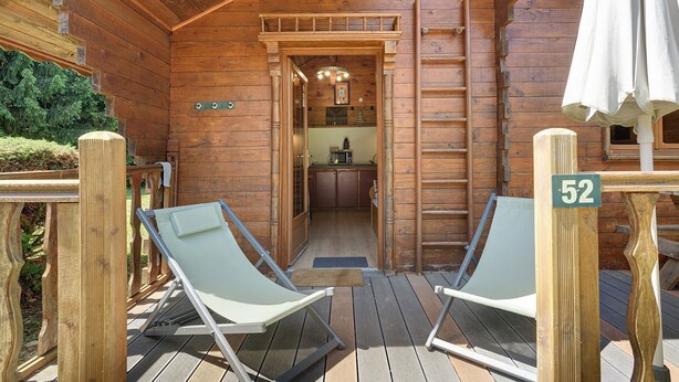 Une cabane en bois dotée d’une terrasse, de deux chaises longues, d’un coin cuisine et d’une pancarte indiquant le numéro de chambre : 52.