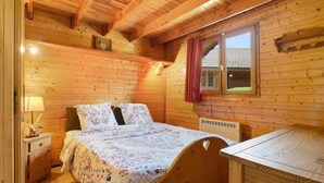 Une chambre à coucher dans une cabane en bois, avec un lit, une table de chevet, une lampe et une fenêtre donnant sur une maison.