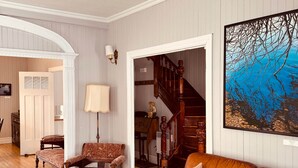 A spacious living room with a brown leather sofa, a patterned armchair, a wooden staircase, and a large framed picture on the wall. - L'Élégante Centenaire de Matane (Matane)