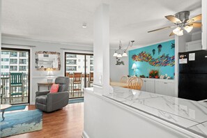 A modern kitchen with a black refrigerator, a dining area with wooden chairs, and a large fish mural on the wall. - 2 BR Ocean View Condo | Myrtle Beach Resort B0514 (Myrtle Beach)
