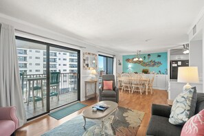 Un salon moderne comprenant un coin repas, une cuisine et un balcon offrant une vue sur l’immeuble.