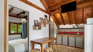 Cocina compacta con armarios de madera, una mesa de comedor con taburetes y una cama en la habitación contigua.