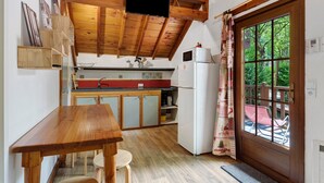 Una cocina con vigas de madera, televisor, refrigerador y ventana con vistas a la vegetación.