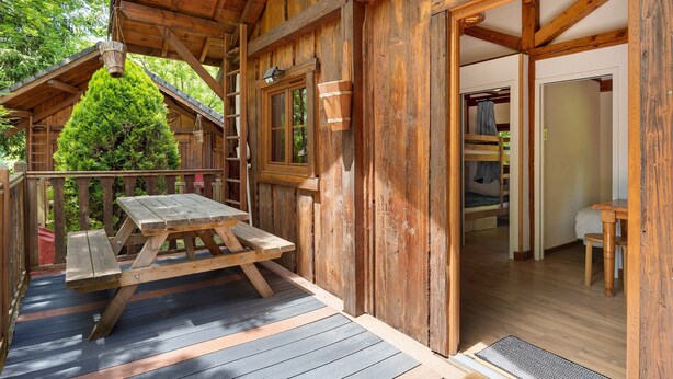 Una cabaña de madera con una mesa de picnic, una escalera y una puerta que da a un dormitorio.