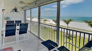 Un balcone con vista sulla spiaggia, una ventola a soffitto e un tavolo con sedie.