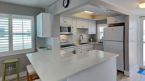 Una cucina moderna con mobili bianchi, un'isola centrale, un forno a microonde, un forno e un frigorifero.